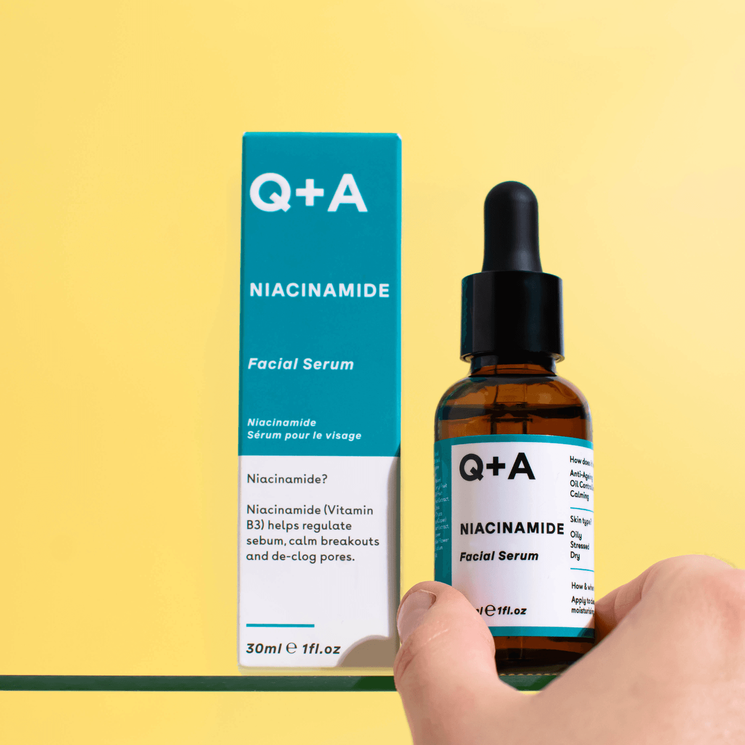 Hand holding Q+A niacinamide serum beside its carton on yellow